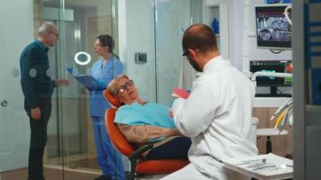 Stomatologist holding plaster model of the mandible speaking with elderly patient. Dentist showing the correct dental hygiene using mock-up of skeleton of teeth, sample of human jaw with toothbrush video