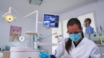 Dentistry doctor talking about dental surgery showing x-ray on monitor unit, patient pov. Stomatology specialist wearing protective face mask pointing at teeth radiography in stomatological clinic video