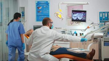 idosos paciente deitado dentro cadeira às a dentista olhando dentro a espelho. estomatologista mostrando a resultado do dental Cuidado depois de higiênico limpeza exame do dentes, conceito do branco saudável sorrir video