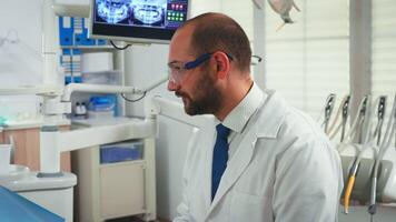 Close up of stomatologist talking with woman in dental clinic. Doctor and nurse working together in modern stomatological office explaining radiography of teeth from digital monitor in background video