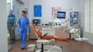 Nurse inviting next patient in stomatology room showing to lie on chair. Dentistry assistant sitting in consultation dental room with elderly woman while doctor speaking with old man in background. video