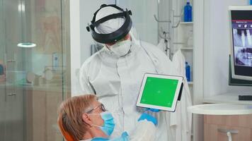 Dentist in coverall pointing at green screen display during coronavirus epidemic. Explaining using monitor with chroma key izolated chroma pc key mockup greenscreen display mock-up touchscreen video