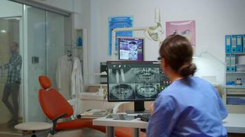 stomatologisch Krankenschwester einladend Mann im Beratung Dental Zimmer während Tippen auf Computer, geduldig warten Arzt zum Prüfung seine Problem. assistent Analysieren Digital Zähne Radiographie im modern Klinik video