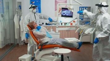 Dentist in protection suit examining teeth with medical instruments in stomatological clinic during global pandemic. Assistant and orthodontic doctor wearing coverall, face shield, mask and gloves. video