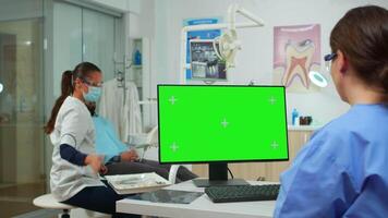 Stomatologist nurse looking at green screen tablet while specialist dentist is examining patient with toothache sitting on stomatological chair. Woman using monitor with chroma key izolated pc key mockup video