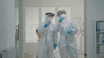 Team of caucasian dentists with hazmat suits discussing prevention for coronavirus at dentistry clinic. Professional stomatology doctors standing in dental cabinet with healthcare equipment video