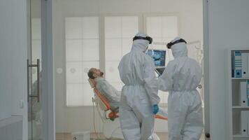 Dental team of dentists consulting patient in cabinet at oral clinic. Caucasian women with dentistry occupation wearing virus protection suits, using stomatology equipment for teeth care video