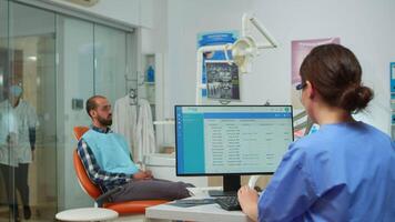 Dentist assistant making appointments on computer while dentistry doctor pointing on digital screen showing dental implants. Stomatologist explaining x-ray of teeth on monitor stomatological clinic. video