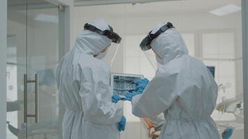 Stomatologists with ppe suits holding digital tablet with teeth x ray analyzing dental healthcare for implant operation at medical clinic. Dentists using scan technology during pandemic video