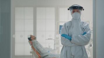 Portrait of caucasian dentist prepared for dental surgery at oral clinic, wearing protection suit with mask, face shield, gloves and coverall. Stomatology specialist looking at camera video