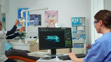 Krankenschwester Arbeiten beim Digital Dental Fingerabdruck von geduldig, während Spezialist Zahnarzt Arzt mit Gesicht Maske ist Sprechen zu Mann mit Zahnschmerzen Sitzung auf stomatologisch Stuhl vorbereiten Werkzeuge zum Untersuchung. video