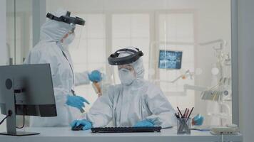 Medical stomatology staff working on teeth healthcare for patient at dental clinic, wearing protection suits. Nurse using modern computer at desk while dentist holding x ray for implant video