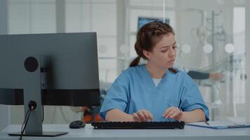 estomatológico assistente digitando em computador teclado sentado às oral clínica escrivaninha. enfermeira usando tecnologia enquanto profissional ortodontista consultando paciente com equipamento dentro fundo video