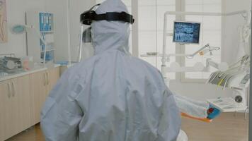 Orthodontist with ppe suit preparing for patient consultation using dental equipment and tools in oral cabinet. Dentist talking to assistant before starting teethcare examination video