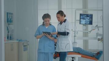 profesional dentista hablando a enfermero y mirando a digital tableta para dientes diagnóstico después examen en dental gabinete. ortodoncia equipo utilizando dispositivo herramienta para odontología cuidado de la salud video