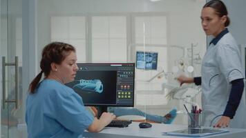 odontoiatria assistente utilizzando computer con virtuale denti animazione mentre dando X raggio scansione per dentista per paziente visita medica nel orale mobiletto. stomatologia squadra con radiografia e tenere sotto controllo video