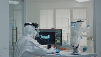 Orthodontists analyzing virtual teeth animation at oral clinic desk. Professional assistant looking at scan on computer monitor while dentist examining model for patient implant video