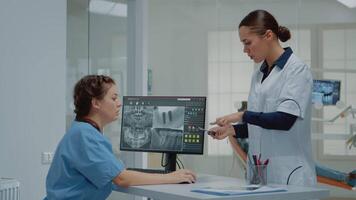 dentista participación dentición X rayo escanear comparando a radiografía en computadora monitor a dental clínica. enfermero sentado a escritorio mirando a pantalla para dientes examen y consulta video