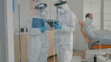 Team of dentists with ppe suits holding tablet for teeth consultation at dental clinic. Orthodontists wearing coverall, face shield and gloves using digital technology for oral care video