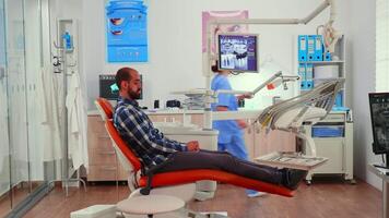 infirmière en mettant dentaire bavoir à homme avant stomatologique examen attendre pour stomatologue médecin en train de préparer patient pour les dents chirurgie. infirmière travail dans moderne orthodontique clinique. video