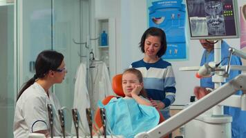 criança usando dedo para ponto afetado dente enquanto a dentista falando com mãe sobre oral dor de dente. odontologia médico explicando para mãe a dental processo, filha sentado em estomatológico cadeira video