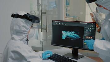 team av ortodontister granskning radiografi av tandläkare på modern dator övervaka på oral klinik. stomatolog och assistent använder sig av dental x stråle skanna för tänder hygien på patient video