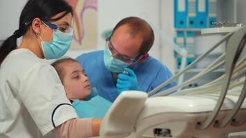 fechar acima Visão do pediatra dentista e assistente limpeza dente para pequeno menina dentro dental clínica sentado dentro estomatológico cadeira. médico e enfermeira trabalhando dentro dental clínica usando esterilizado ferramentas. video