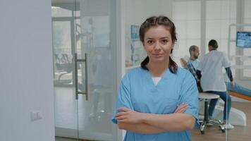 Portrait of dentistry assistant looking at camera standing at stomatology clinic. Caucasian woman with nurse occupation working in dental office wearing medical uniform for teethcare video
