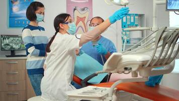 Little girl patient sitting in stomatological chair in dental office, visiting doctor for oral problems. Woman dentist with protective gloves and mask removes tooth decay drilling teeth during surgery video