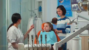 Pediatric woman dentist treating little girl patient in modern stomatological dentistry office showing teeth x-ray explaining to mother dental intervention. Visiting dentist with children. video