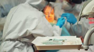 médico equipo trabajando con esterilizado herramientas vistiendo cara proteger, bata traje, máscara y guantes durante coronavirus brote en nuevo normal estomatológico clínica. dentista tratando dientes de pequeño niña video