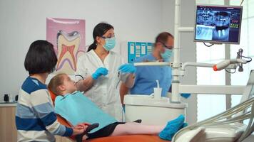 pediátrico enfermero y dentista médico trabajando en moderno dental clínica tratando pequeño niña paciente con dolor de muelas sentado en estomatológico silla. mamá visitando estomatólogo con niños consultante masa video