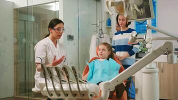 Mother visiting dentistry clinic with kid having medical treatment, speaking with stomatologist. Dentist talking with child sitting on stomatological chair while nurse preparing sterilized tools. video