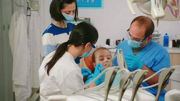 Child sitting in stomatological chair opening mouth for exemination, in dental office, visiting doctor for oral problems. Pediatric dentist with mask removes tooth decay drilling teeth during surgery video