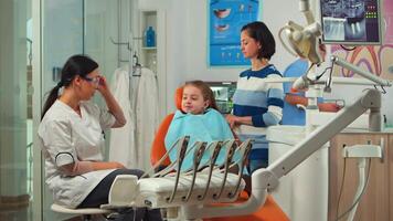 estomatologista segurando gesso modelo do a mandíbula Falando com menina paciente. dentista mostrando a corrigir dental higiene usando brincar do esqueleto do dentes, amostra do humano mandíbula com escova de dente video