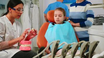 Pediatric stomatologist explaining to little patient procedure of extraction using model of dental teeth. Doctor holding sample of human jaw telling informations for keeping healthy teeth, digital x-ray in background video