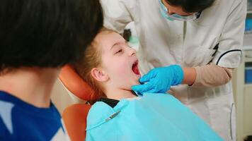 proche en haut de fille patient mensonge sur stomatologique chaise avec ouvert bouche pendant dentaire examen. stomatologue avec masque en portant stérilisé outils vérification les dents santé de enfant avant intervention. video