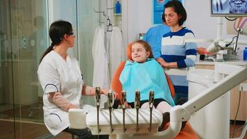 Stomatologist explaining dental treatment holding radiography pointing on affected teeth while man assistant preparing sterilized tools for surgery. Doctor and nurse working in stomatological unit video