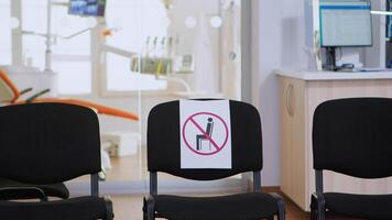 Empty waiting area, stomatology reception with nobody in it with new normal having sign on chair for social distance during covid-19 epidemic. Dental waiting room modern equipped in outbreak time video