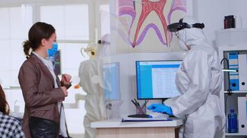 Woman with face mask coming in dental clinic to check teeth health during coronavirus pandemic. Concept of new normal dentist visit in covid-19 outbreak wearing protective suit and face shield video