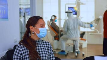 Portrait of young woman with protection mask discussing sitting on chairs keeping social distance in stomatological clinic, waiting for doctor during coronavirus. Concept of new normal dentist visit video