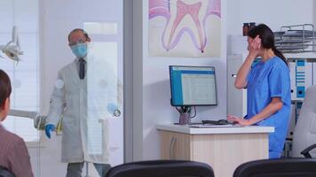 dentiste finition avec vieux homme, demander infirmière pour suivant dentaire radiographie pendant les patients en attendant. orthodontiste et infirmière travail dans bondé moderne stomatologique clinique, stomatologue à la recherche à radiographie video