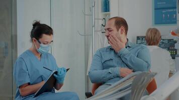 patient expliquant mal aux dents à dentisterie infirmière à stomatologie visite. orthodontique assistant prise Remarques à préparer pour oral se soucier procédure à guérir carie douleur avec dentaire outils dans armoire. video