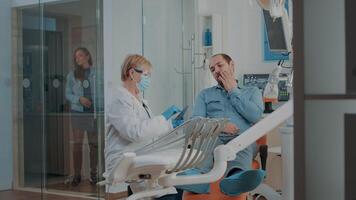 tandläkare ser på dental x stråle och hört patient med tandvärk, analyserar radiografi skanna till do borra procedur. stomatologisk specialist håller på med oral vård hålighet undersökning. video