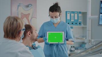 Nurse and patient analyzing green screen on digital tablet in dentistry cabinet. Dental assistant looking at blank chroma key with mock up template and isolated background on copy space gadget. video