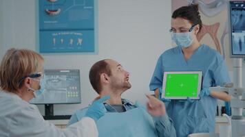 Patient and dentistry team looking at tablet with green screen. People in stomatology cabinet using isolated template with mockup copy space and chroma key background on digital device. video