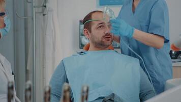 paciente com oxigênio mascarar recebendo anestésico dentro odontologia gabinete, obtendo pronto para estomatológico procedimento com dental Ferramentas e broca para polonês cárie. oral Cuidado anestesia em cara. video