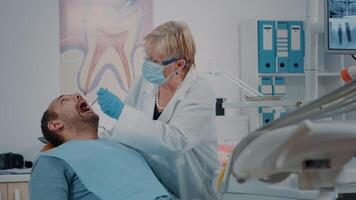 oral cuidado médico utilizando dental herramientas a hacer dientes examen en odontología gabinete. mayor dentista analizando dentadura después cirugía procedimiento a cura dolor de muelas y cavidad problemas. video