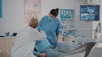 Dentist doing oral care examination on patient with toothache, using dental tools and instruments in stomatology office. Dentistry expert and nurse consulting teeth at appointment. video