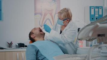 Patient opening mouth and dentist examining dentition work after surgery. Stomatologist doing oral care consultation with instruments, treating man at stomatology checkup appointment. video